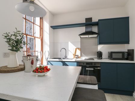 A kitchen with dark blue cabinets a white countertop a black oven and microwave with strawberries and a bottle on the counter at Llety Pen Deitsh 1 in Caernarfon