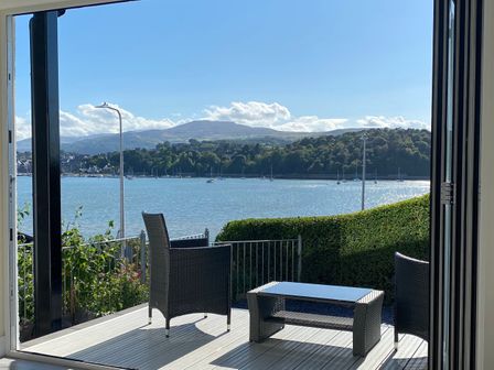 A patio with two chairs and a table overlooking a body of water with hills in the background at The Old Tywyn Post Office in Deganwy