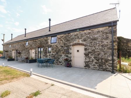 An outdoor patio area with tables, chairs, potted plants, and a stone building with multiple doors and windows at Stabal in Rhosneigr