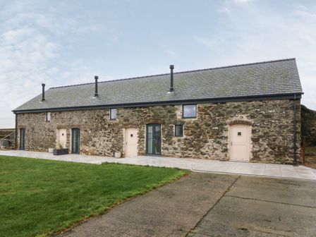 Exterior of a stone building with multiple doors and windows on a concrete patio with grass in front at Beudy in Llangefni