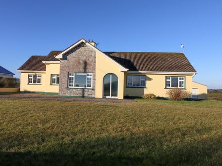 A single story house with yellow walls and a tiled roof on a grassy lawn at Mullagh Road in Miltown Malbay County Clare