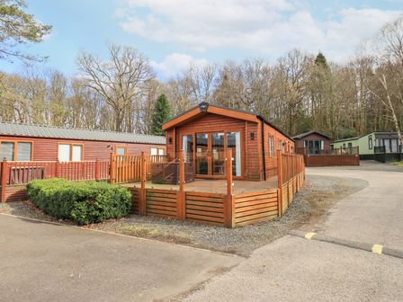 A wooden lodge with glass doors and a fenced deck in a park with other lodges and trees at Windermere View Pony Meadow 37 White Cross Bay near Windermere