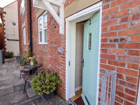 An open light blue door numbered 2 on a red brick building beside a small table with chairs and plants at Tuksumduin in Whitby