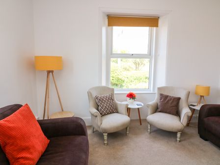 A seating area with two beige armchairs and two brown sofas with cushions beside a window at Thornlea View in Hope Cove