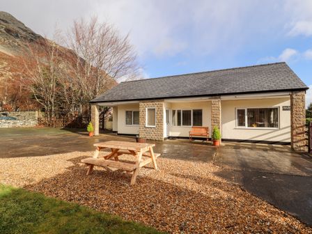 A single-story house with a patio bench and a wooden picnic table on gravel at Awel Y Berwyn in Llangynog