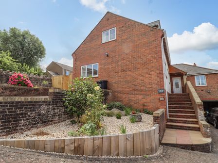 An outdoor view of a brick house with stairs leading to a white door and a garden with plants and flowers at Corner House in Cinderford