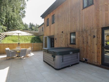 An outdoor patio with a hot tub wood siding on the house a table with chairs and an umbrella at Stag Cottage in Lytchett Matravers