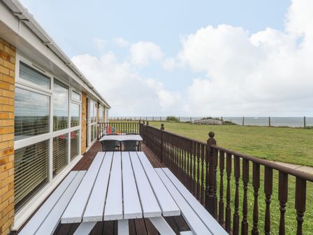 A patio with white picnic tables and chairs next to a grass field and a fenced area at Bungalow 14 in Corton