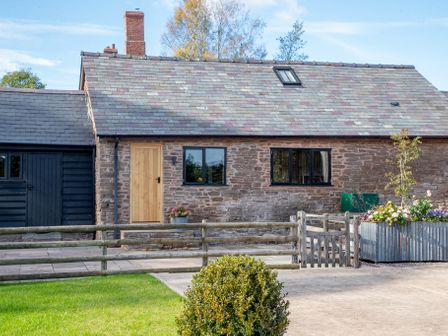 A stone house with a wooden door two windows a wooden fence and a planted flower bed at Frith Green in Pencombe near Bromyard