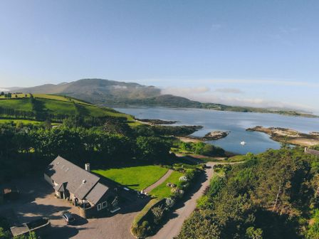 A house with a grey roof near a body of water surrounded by green hills and trees at Inbear Sceine in Laughaunacreen near Tuosist County Kerry