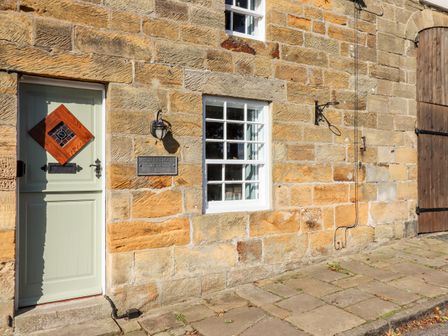 Front view of a stone cottage with a light green door and white-framed window at Michaelmass Cottage in Castleton