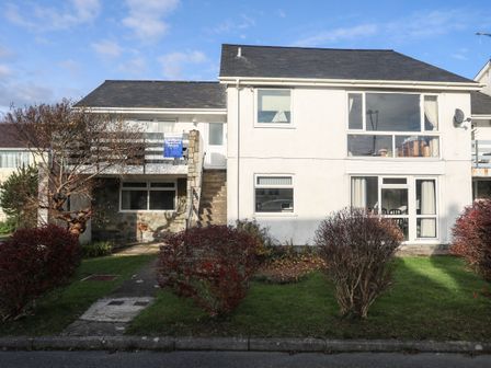 A two story white house with bushes and trees in the front garden at 5 Ger Y Nant in Llanbedrog
