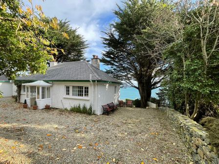 A small white cottage with a slate roof surrounded by trees and benches overlooking the sea at Rocklea Seaside Cottage in Newcastle County Down
