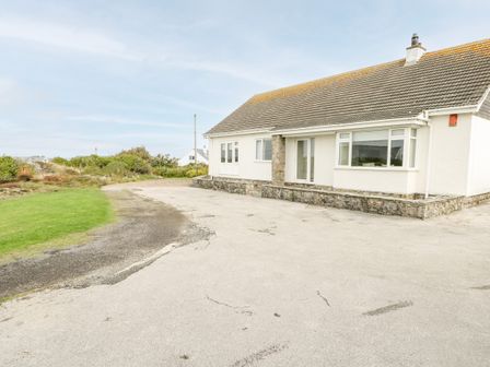 A single-story house with a tiled roof and stone accents by a paved driveway and grassy area at Moorside in Trearddur Bay