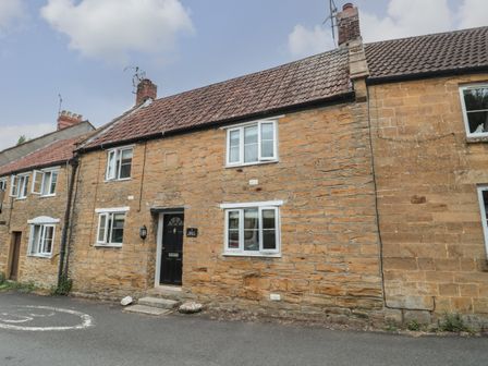 A stone house with tiled roof black front door and multiple white framed windows at Holly Cottage in West Coker