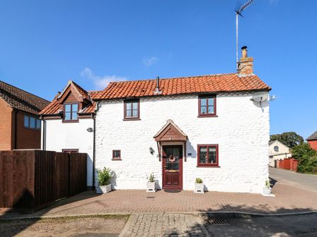 A white stone cottage with red roof tiles and wooden windows on a paved area