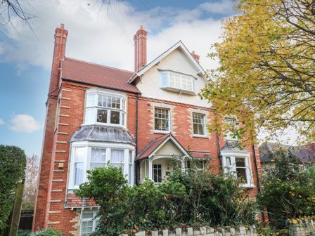 A large brick house with white framed windows and a red roof surrounded by trees and bushes at Bayview Loft in Weymouth