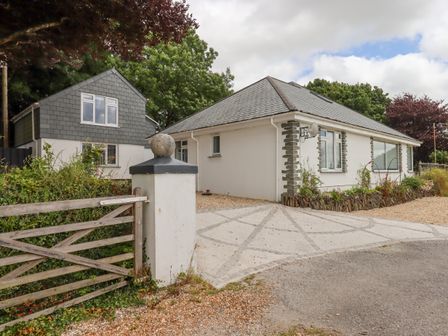 A driveway with a wooden gate and two houses with gray roofs surrounded by trees at Hurdwick Lodge in Tavistock