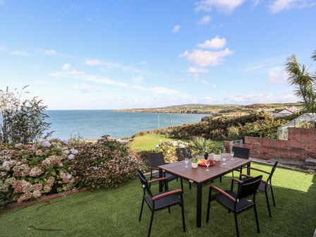 An outdoor patio with a table and six chairs overlooking the sea at Ser a Mor Stars and Sea in Bull Bay near Amlwch