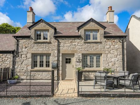 Stone cottage with two chimneys and outdoor seating area at Lleiniog Cottage in Beaumaris