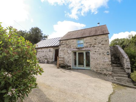 An exterior view of a stone house with two entrances and outdoor stairs surrounded by greenery at Y Felin at Coed Cadw in Felindre Farchog near Newport Pembrokeshire