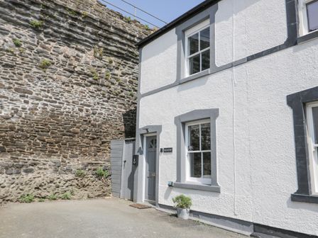 A white house with gray trim near a stone wall with a potted plant by the door at Havens End in Conwy