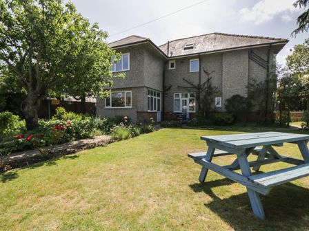 A garden with a tree a flower bed and a wooden picnic table outside a two story house at Molly's Place in Boscombe
