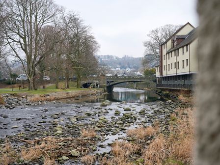 A river with rocks and dry grass a bridge and a building beside the river at Riverside Park 2 in Keswick