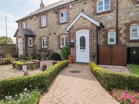 A stone cottage with a white front door and a paved pathway bordered by trimmed hedges at Knapp Cottage in Chickerell