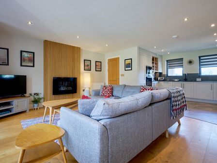 An open-plan living room and kitchen with a grey sofa and wooden tables at Riverside Park 4 in Keswick