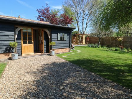 A garden with green grass pebble pathway and wooden building with open doors at The Forge in Old Newton near Stowmarket