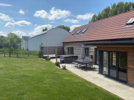 A patio with outdoor dining furniture and hot tub next to a lawn and wooden house at The Gully in Sherborne