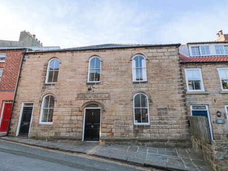 Stone building with arched windows and black doors on a street at Bethel Chapel in Staithes