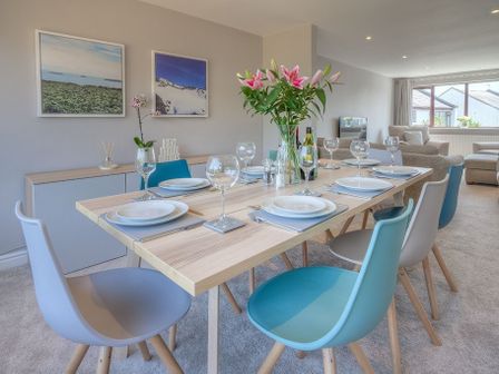 A dining table set with plates and glasses with flowers in a vase in a living room at Cromlin Glas in Abersoch