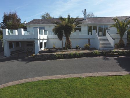 A white house with outdoor stairs palm trees and a driveway at 3 Madoc View in Bwlchtocyn near Abersoch
