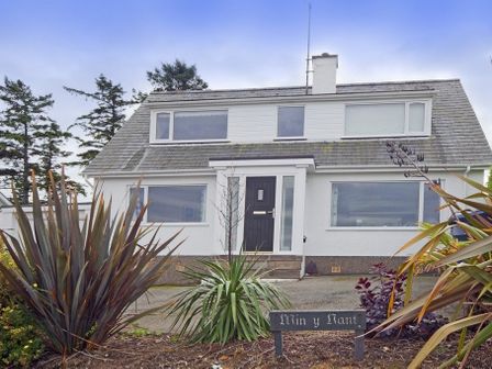 A two-story house with large windows and a black front door surrounded by plants and a sign reading Min y Nant in Abersoch