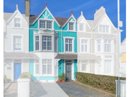 A row of terraced houses with a turquoise house in the center and a driveway in front at Preswylfa in Abersoch