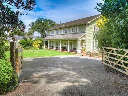 A two-story house with a covered porch and outdoor seating surrounded by trees and bushes at The Coach House in Abersoch