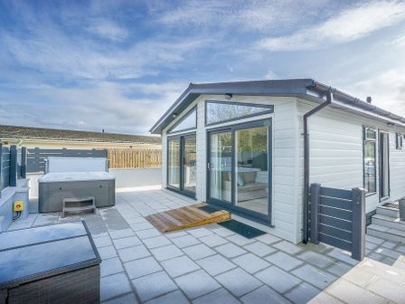 An outdoor patio area with a hot tub sliding glass doors and a small gate at The Warren T23 in Abersoch