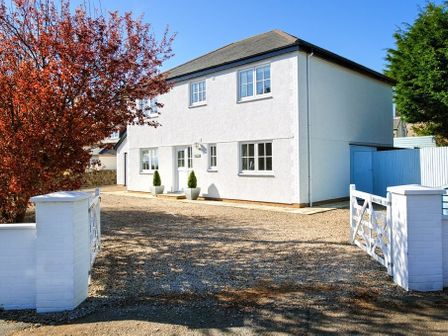 A white two-story house with multiple windows a gravel driveway a white gate two potted plants and a tree with red leaves at Ty Coed in Abersoch