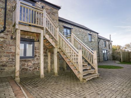 Exterior view of a stone building with wooden stairs leading to an upper door and paved ground at Beacon Barn in St Agnes