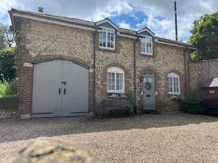 A stone and brick house with arched windows a green door a bench and gravel driveway at The Coach House at Lackington Farm in Piddletrenthide