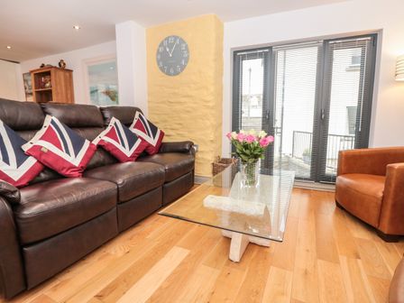 A living room with a brown leather sofa with union jack pillows a glass coffee table with flowers and a brown armchair at 6 The Sail Loft Dartmouth