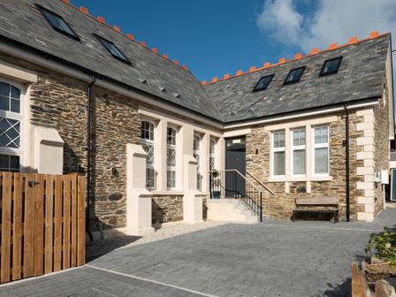 An exterior view of a stone building with multiple windows a wooden gate steps leading to a door and a bench outside at Church Rooms Port Isaac