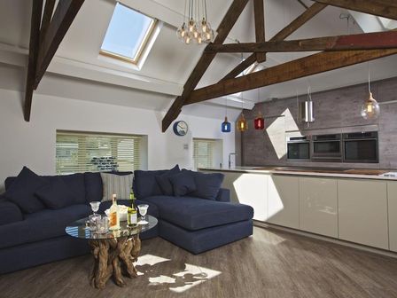 A living area with a dark blue sectional sofa and a glass coffee table with bottles and glasses under exposed wooden beams at The Barn 20 At The Beach in Torcross