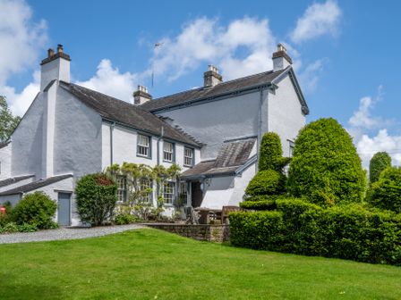 A white house with multiple chimneys and trimmed bushes in the garden at Low Graythwaite Hall in Hawkshead