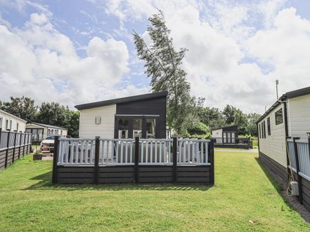 A small modern cabin with a fenced porch on a grassy lot at Yealands 27 in South Lakeland Leisure Village near Carnforth