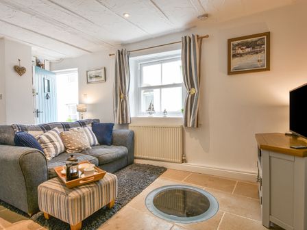 A living room with a grey sofa and striped curtains with a wooden TV stand at Honeymoon Cottage in Appledore