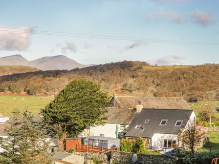 A rural house with sloped roofs surrounded by trees and fields with hills in the background at Brookside in Grizebeck