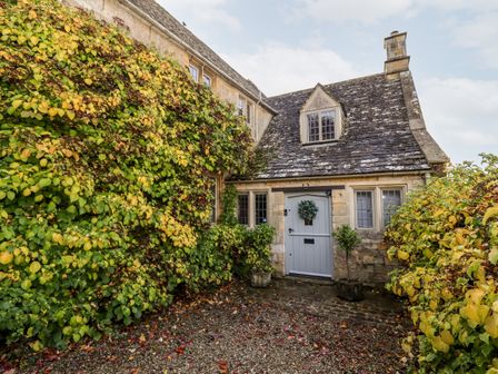 Stone house with a grey door and windows surrounded by green and yellow foliage at The Small House Near Bourton-On-The-Water